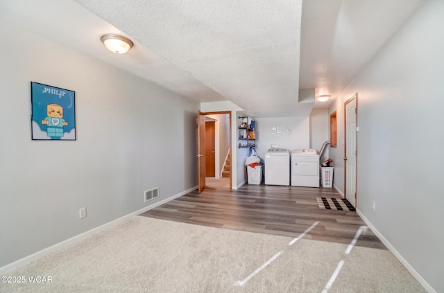 finished below grade area featuring washing machine and clothes dryer, visible vents, baseboards, stairway, and a textured ceiling