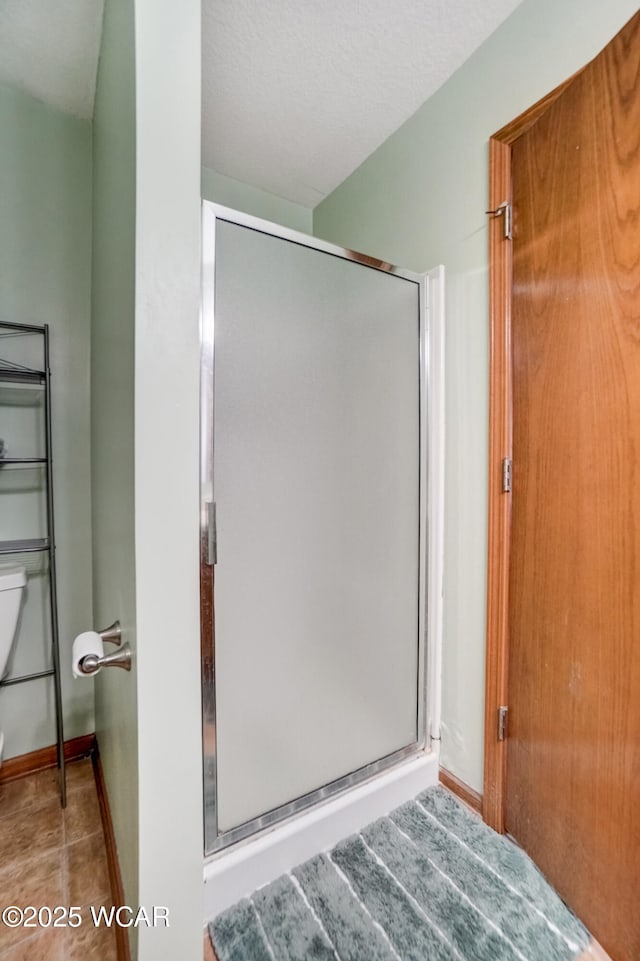 bathroom featuring baseboards, toilet, a shower stall, and a textured ceiling