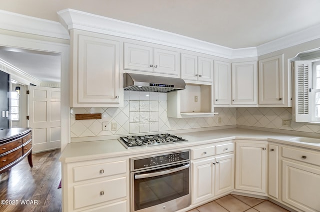 kitchen with appliances with stainless steel finishes, ventilation hood, white cabinetry, backsplash, and ornamental molding