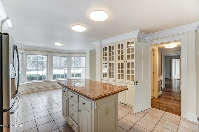 kitchen with light tile patterned floors, ornamental molding, stainless steel refrigerator, and a kitchen island