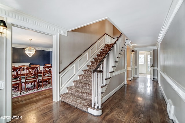 stairs with ornamental molding, wood-type flooring, and a notable chandelier