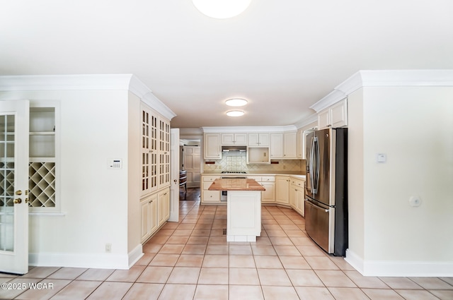 kitchen with light tile patterned floors, crown molding, stainless steel fridge, a kitchen island, and decorative backsplash