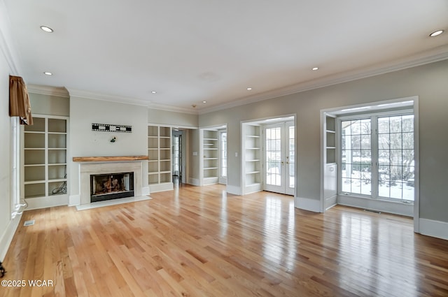 unfurnished living room featuring built in shelves, a high end fireplace, crown molding, and french doors