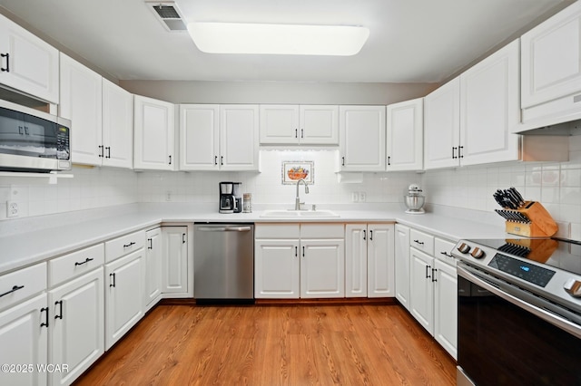 1129 W Bluelick Rd, Lima, OH 45801 - kitchen featuring appliances with stainless steel finishes, tasteful backsplash, light wood-style floors, light countertops, and white cabinetry