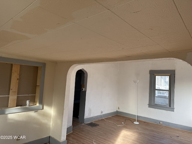 empty room with wood finished floors, baseboards, and arched walkways