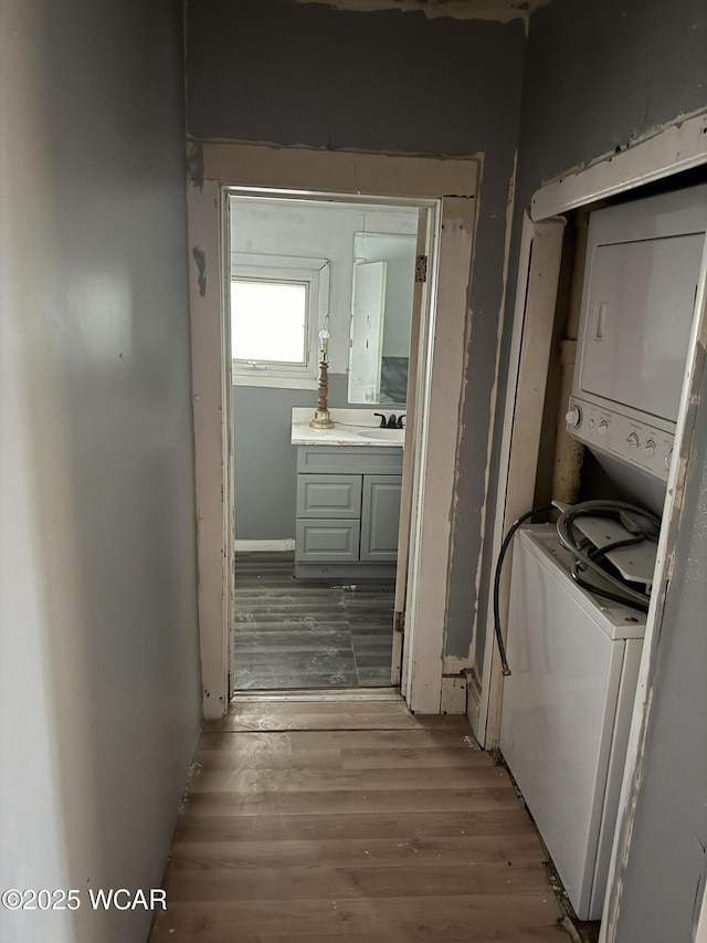 clothes washing area featuring stacked washer and dryer, laundry area, a sink, and wood finished floors