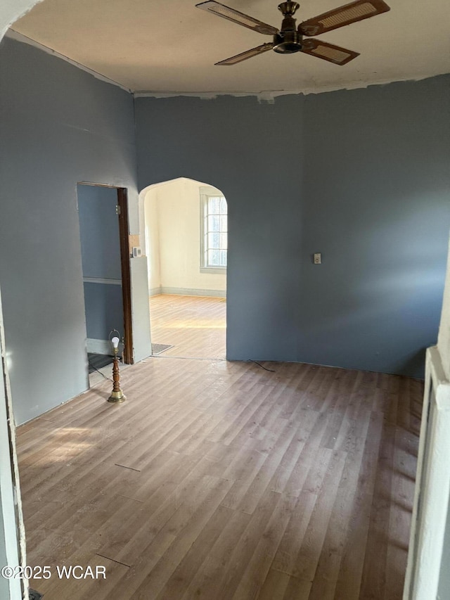 empty room with arched walkways, ceiling fan, and wood finished floors
