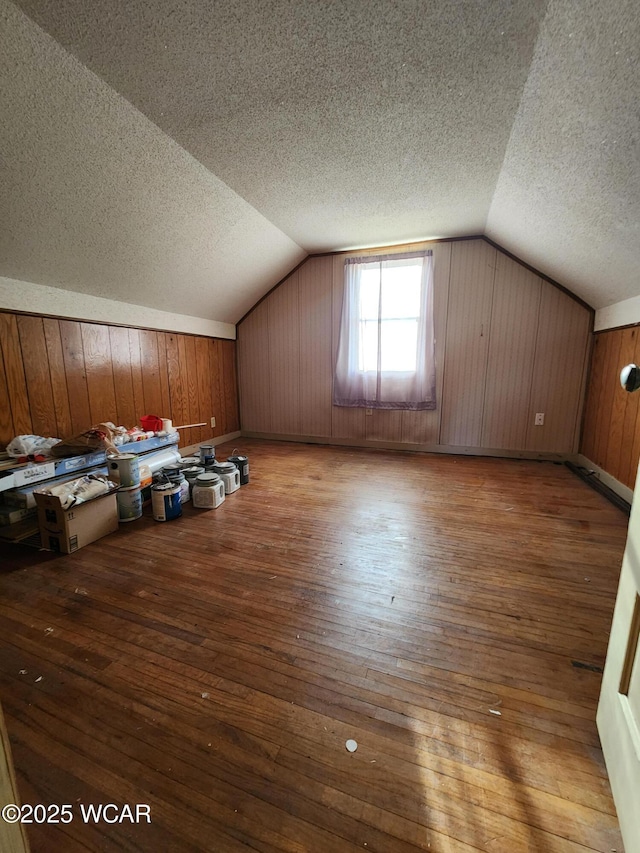 bonus room featuring lofted ceiling, hardwood / wood-style floors, a textured ceiling, and wood walls