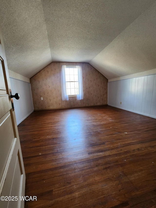 bonus room with lofted ceiling, dark hardwood / wood-style floors, and a textured ceiling