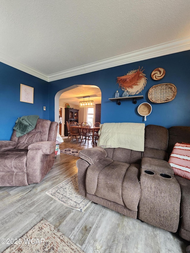 living area featuring ornamental molding, a textured ceiling, arched walkways, a notable chandelier, and wood finished floors