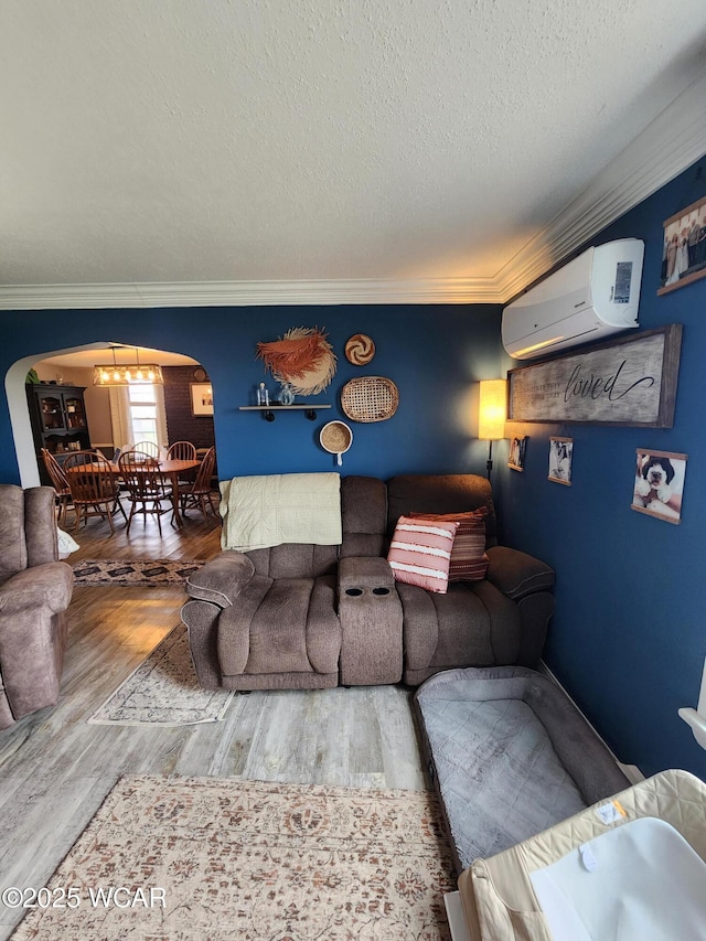 living room featuring a wall mounted air conditioner, a textured ceiling, crown molding, wood finished floors, and arched walkways