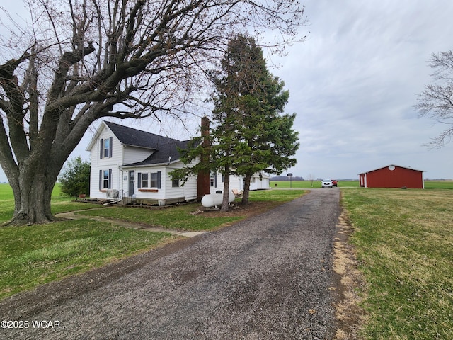 view of side of home featuring an outdoor structure, a lawn, a shingled roof, and a chimney
