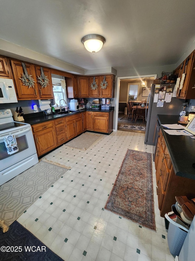 kitchen featuring white appliances, a sink, dark countertops, brown cabinets, and light floors