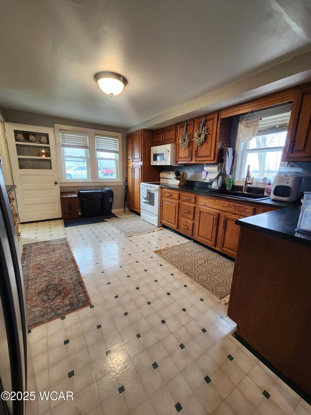 kitchen with a sink, dark countertops, light floors, and white appliances