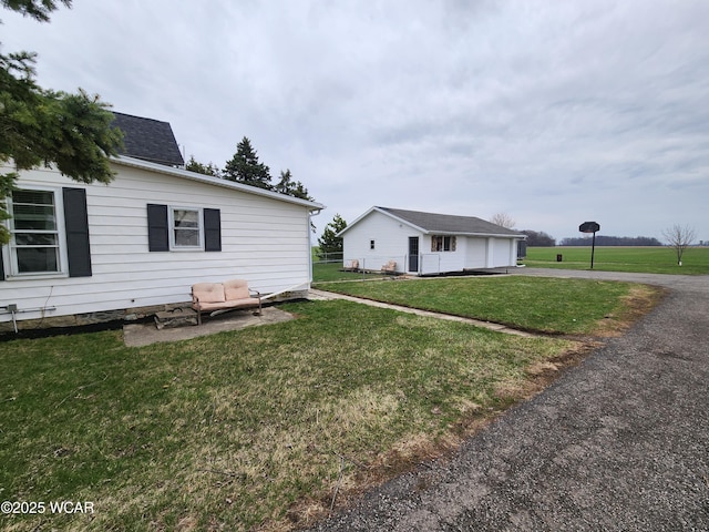 view of side of home featuring a lawn, an outdoor structure, a garage, and aphalt driveway