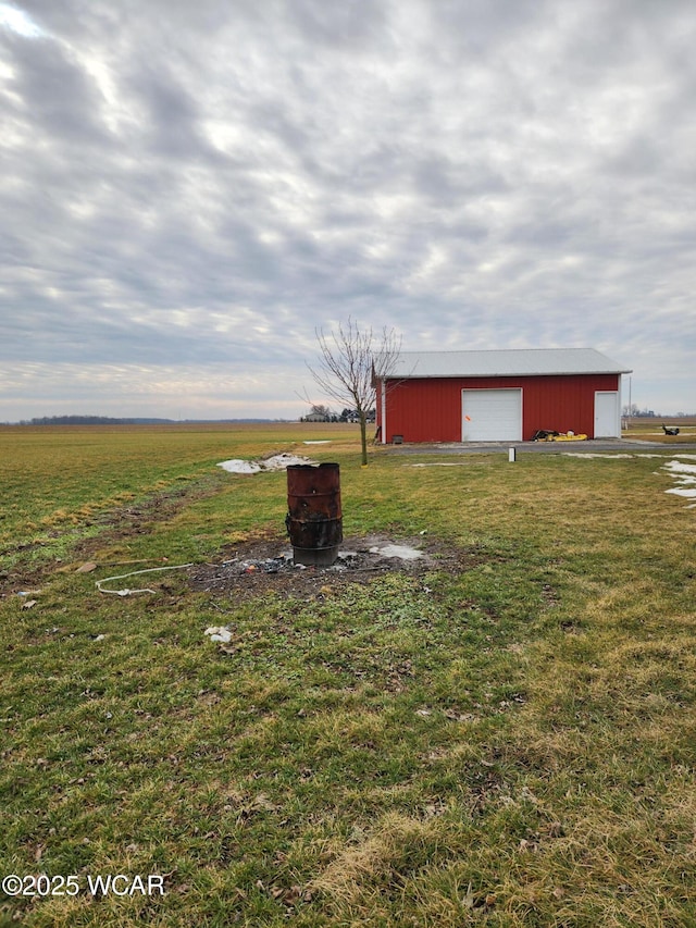 view of yard featuring a rural view, a garage, and an outbuilding