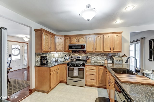 kitchen with appliances with stainless steel finishes, sink, dark stone countertops, and backsplash