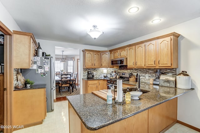 kitchen with sink, dark stone countertops, appliances with stainless steel finishes, kitchen peninsula, and decorative backsplash