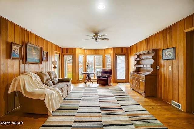 living room with wood walls, ceiling fan, and light hardwood / wood-style flooring