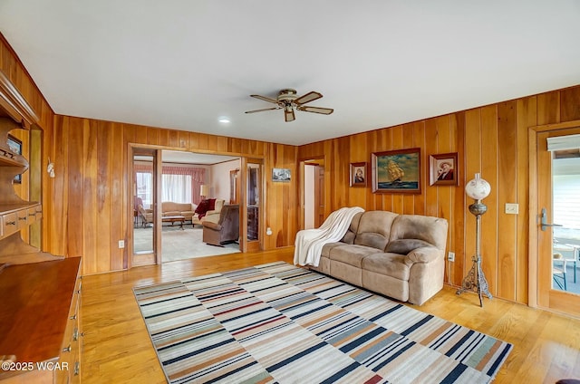 living room with ceiling fan, wooden walls, and light hardwood / wood-style floors