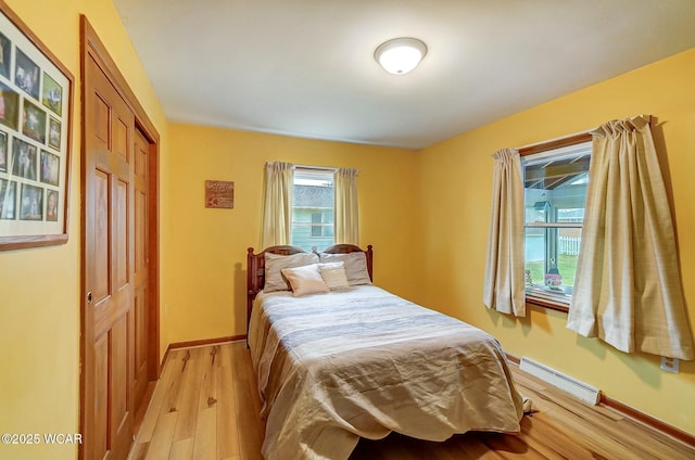 bedroom with light wood-type flooring, baseboard heating, and a closet