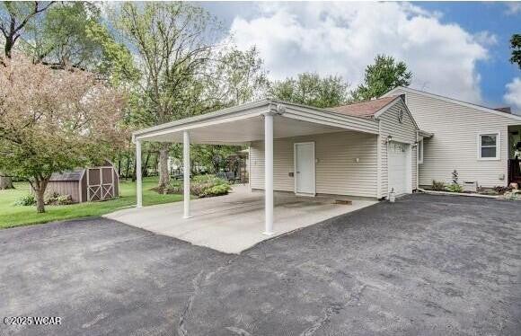 exterior space featuring a storage unit, a carport, an attached garage, and aphalt driveway