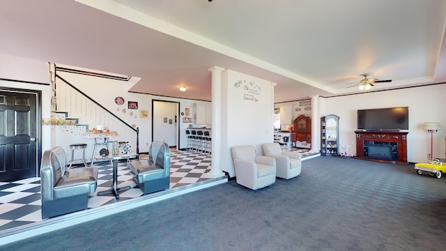 carpeted living room featuring a raised ceiling, decorative columns, a ceiling fan, and a fireplace with raised hearth