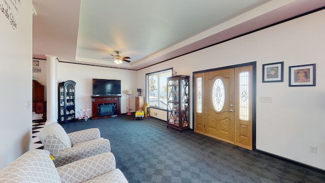 entryway featuring a tray ceiling, dark carpet, a fireplace, baseboards, and ceiling fan