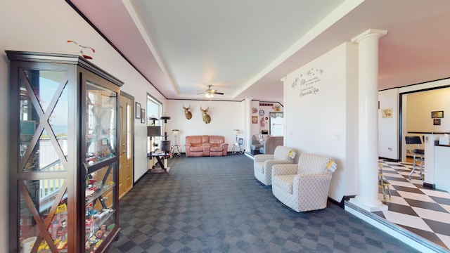 living area featuring carpet floors, a tray ceiling, decorative columns, ceiling fan, and tile patterned floors