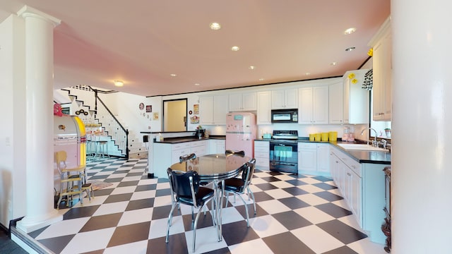 kitchen featuring black appliances, decorative columns, light floors, and a sink