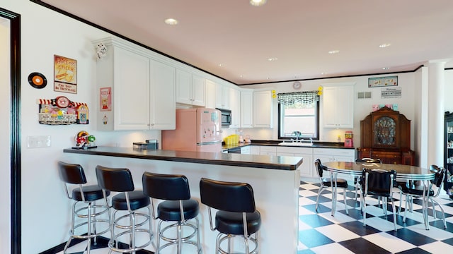 kitchen featuring light floors, a peninsula, freestanding refrigerator, a sink, and dark countertops