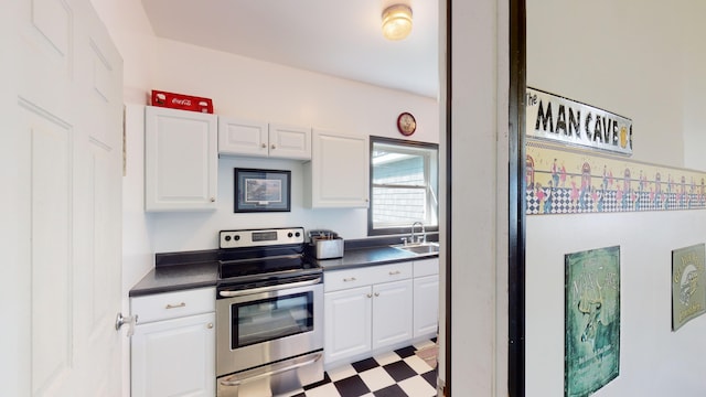 kitchen with tile patterned floors, a sink, dark countertops, white cabinetry, and stainless steel electric range oven