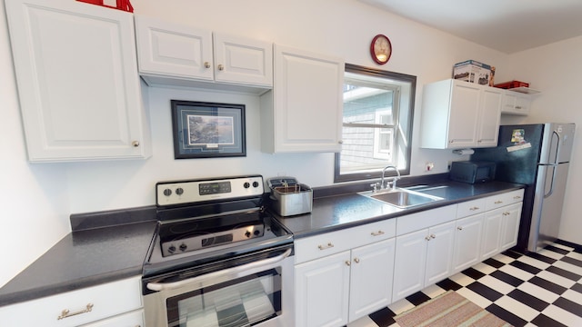 kitchen with light floors, a sink, stainless steel appliances, white cabinetry, and dark countertops