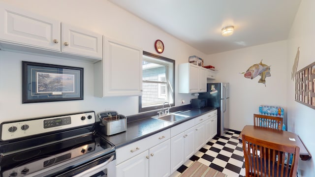 kitchen with dark countertops, light floors, appliances with stainless steel finishes, white cabinetry, and a sink