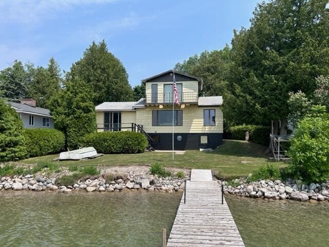 dock area featuring a water view, a lawn, and a balcony