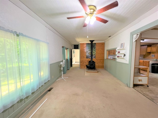 interior space featuring visible vents, wooden walls, ceiling fan, a wainscoted wall, and a wood stove