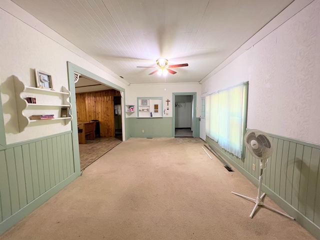 carpeted empty room featuring wooden walls, ceiling fan, and wainscoting