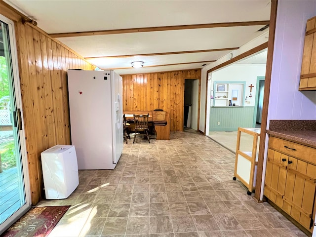 kitchen with dark countertops, beamed ceiling, white refrigerator with ice dispenser, and wood walls