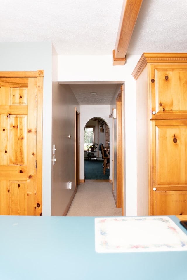 hallway with beamed ceiling, arched walkways, and light colored carpet