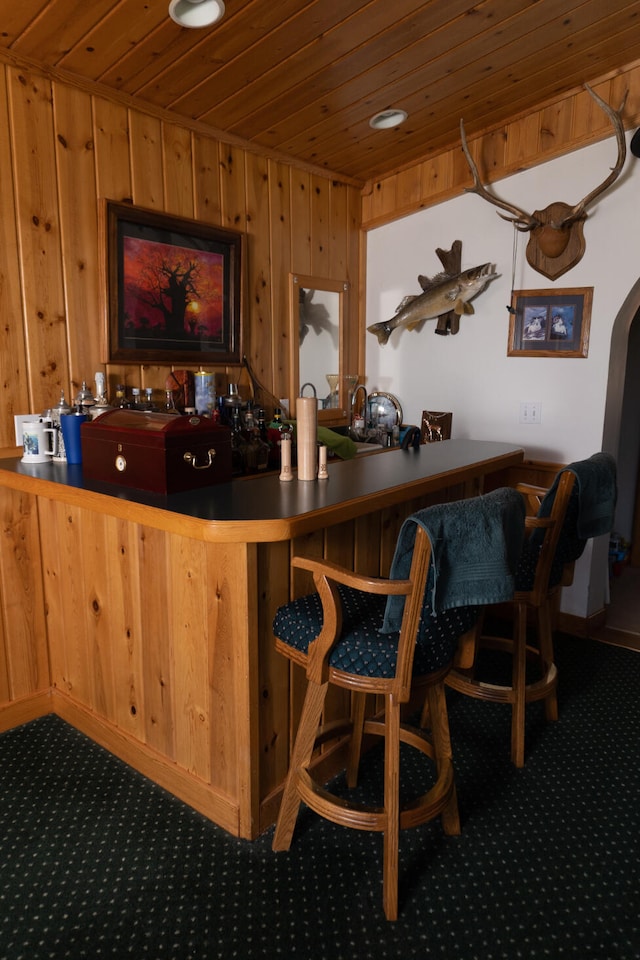 bar with carpet floors, wet bar, arched walkways, wood ceiling, and wood walls