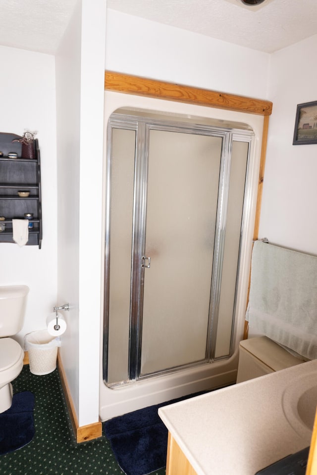 bathroom featuring a shower with door, baseboards, and toilet