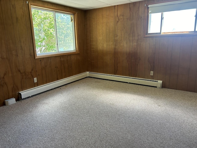 spare room with wooden walls, a drop ceiling, a baseboard radiator, and carpet floors