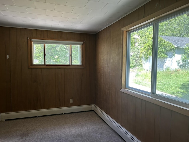 carpeted empty room featuring plenty of natural light, baseboard heating, wooden walls, and a baseboard radiator