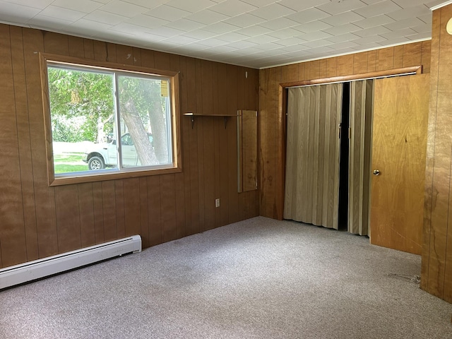 unfurnished bedroom with a baseboard radiator, a closet, wood walls, and carpet flooring