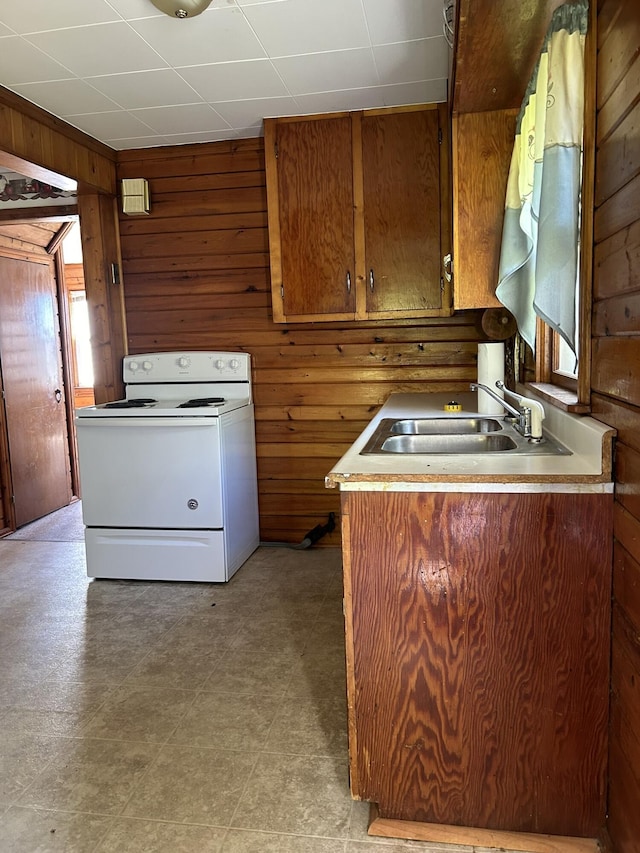 kitchen with a sink, brown cabinets, wood walls, and white electric stove