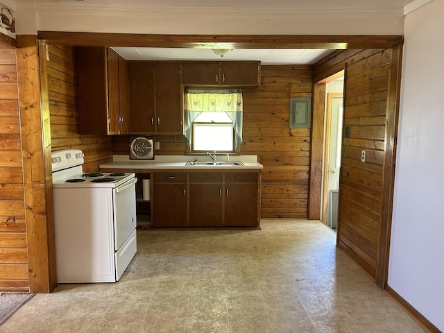 kitchen with white range with electric cooktop, a sink, wood walls, light countertops, and light floors