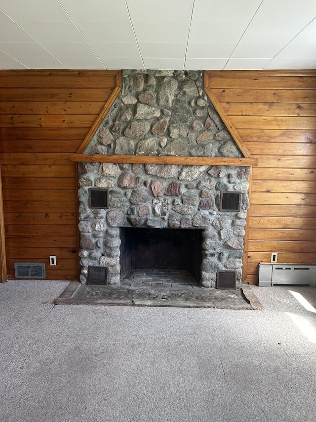 unfurnished living room featuring a stone fireplace, visible vents, carpet floors, and wood walls