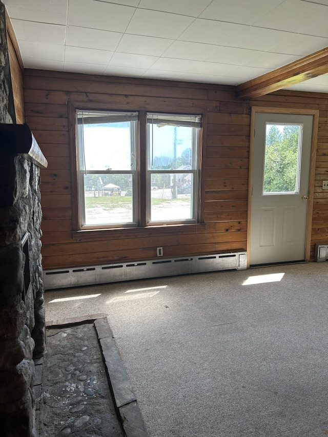 empty room featuring carpet floors, baseboard heating, and wooden walls