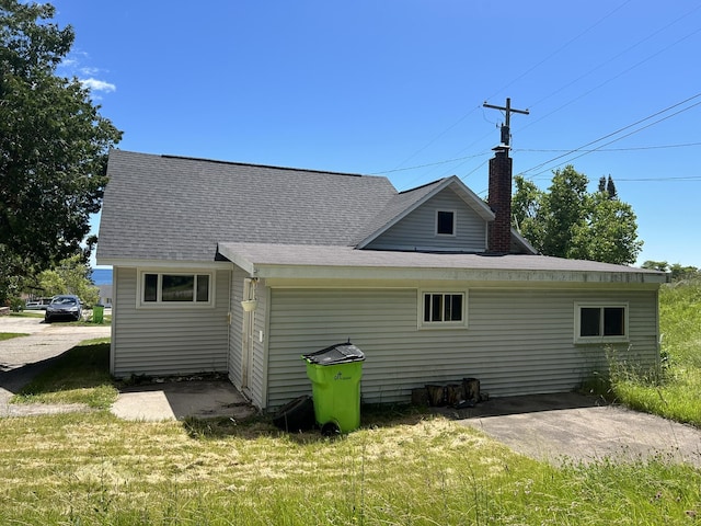 rear view of property featuring a lawn, a chimney, and roof with shingles