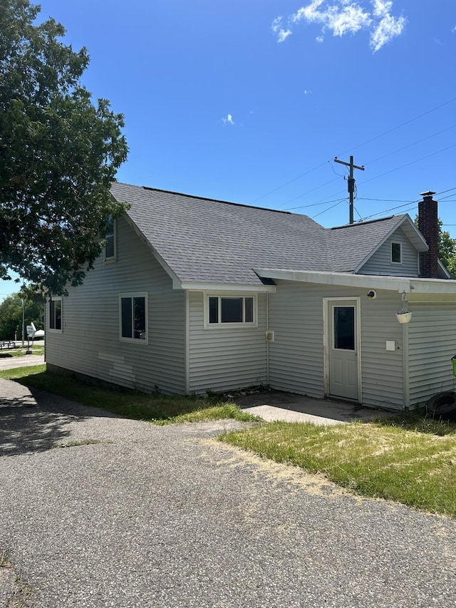 rear view of house featuring a chimney and a shingled roof